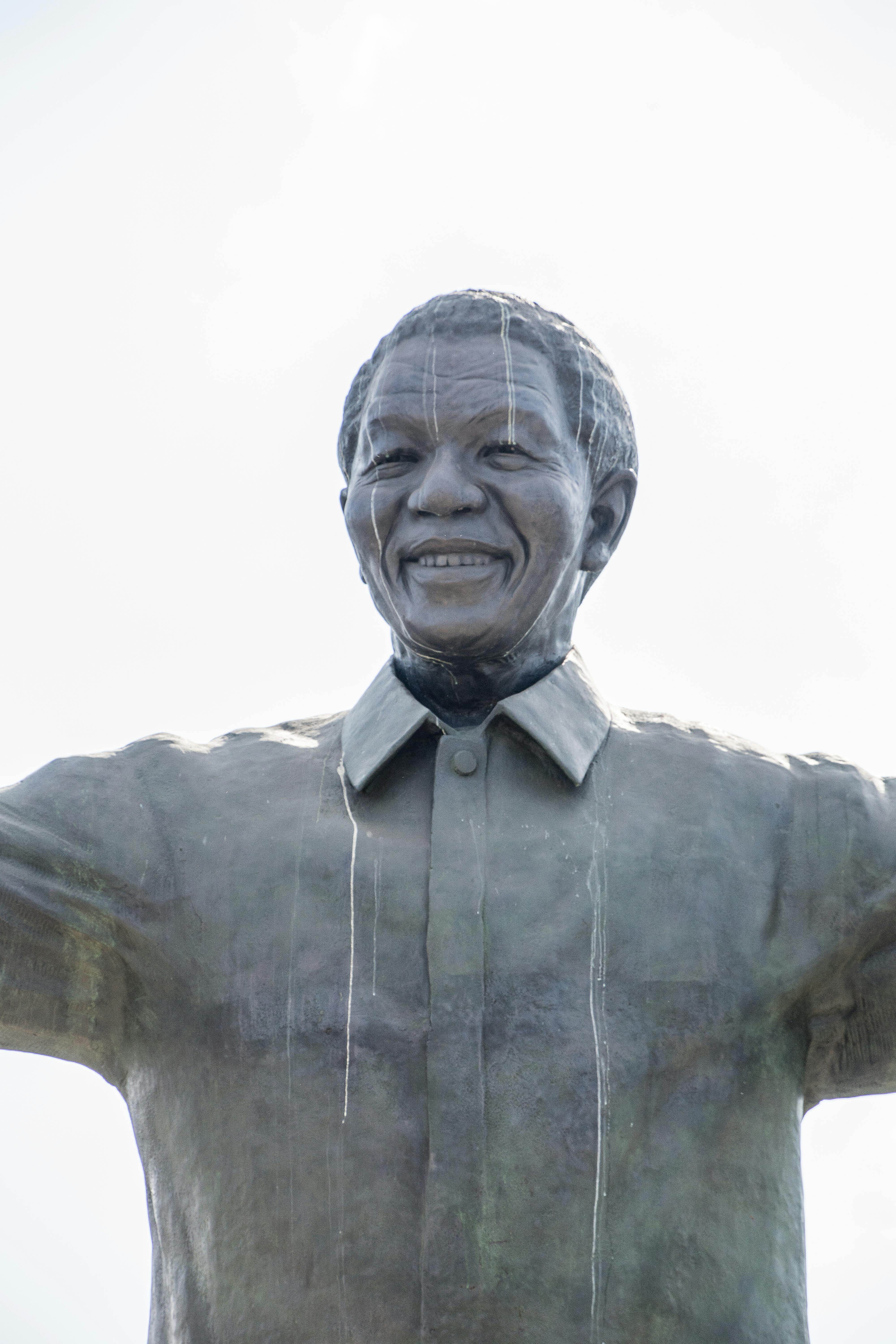 Close-up of Nelson Mandela statue with arms raised, set against a bright sky.